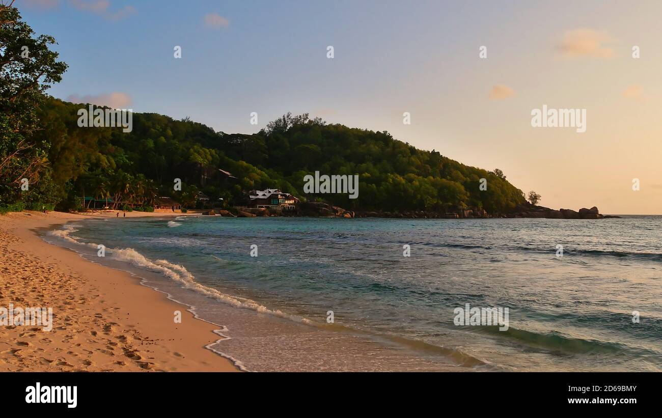 Spiaggia tropicale Anse Takamaka nel sud di Mahe, Seychelles con sabbia, acqua calma, palme, foresta pluviale e alloggio turistico in serata. Foto Stock