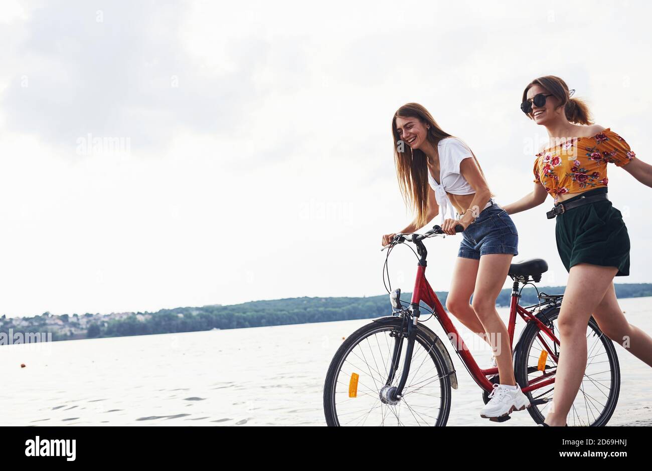 Due amiche in bicicletta si divertono in spiaggia vicino al lago Foto stock  - Alamy