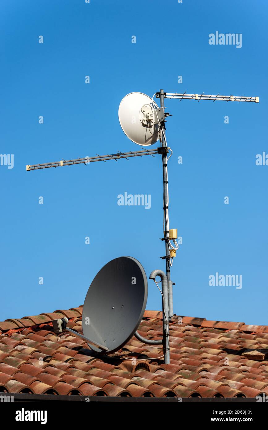 Primo piano di una antenna televisiva e di un piatto satellite sul Casa tetto su un cielo blu chiaro Foto Stock