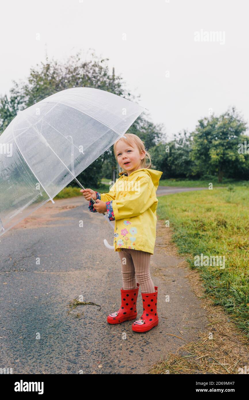 Divertente bambina che gioca in giardino sotto la pioggia autunnale.  Bambino che indossa giacca impermeabile gialla e stivali che tengono  ombrello colorato. Tempo piovoso Foto stock - Alamy