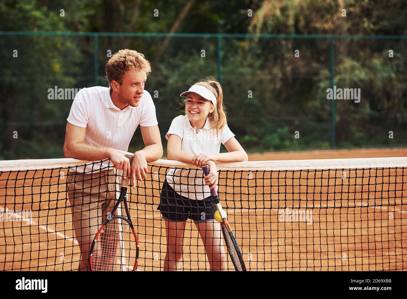 Prendendo una rottura appoggiandosi sulla rete. Due persone in uniforme sportiva giocano a tennis insieme sul campo Foto Stock