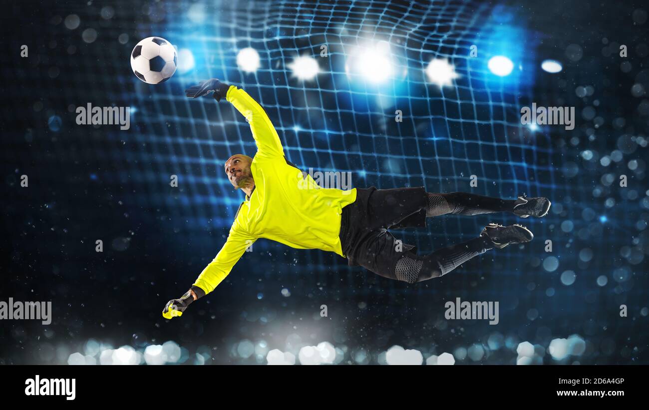 Portiere di calcio, in uniforme fluorescente, che fa un grande risparmio ed evita un goal su uno sfondo blu scuro Foto Stock