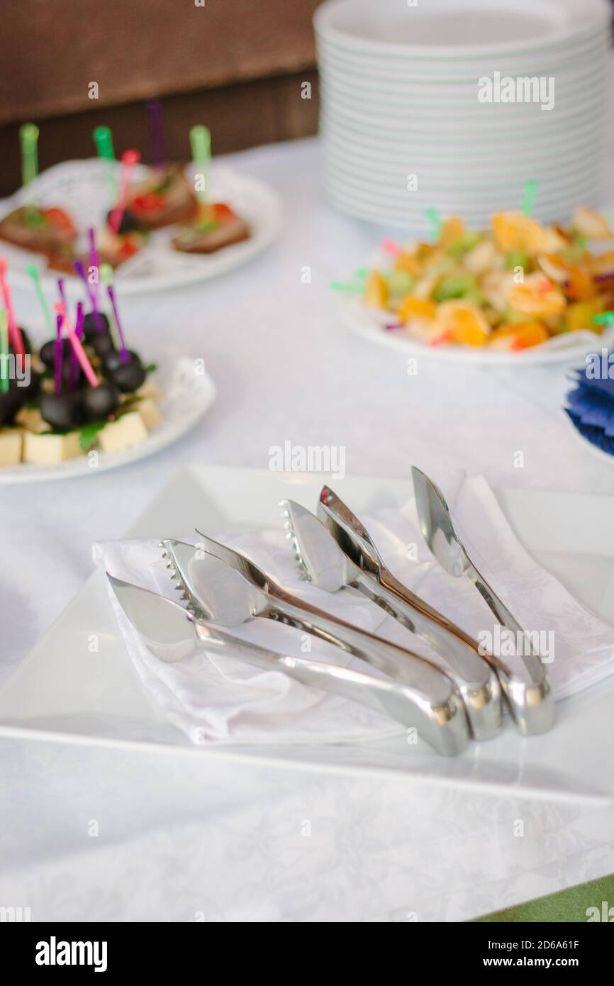 attrezzature per il servizio catering - pinze metalliche su piastra bianca. Foto Stock