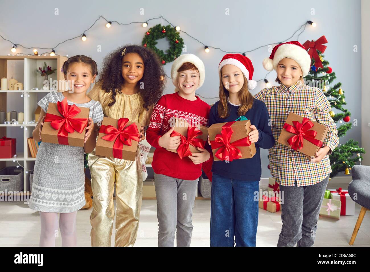 Felici e diversi bambini che tengono regali di Natale in piedi in un accogliente soggiorno durante la festa a casa Foto Stock