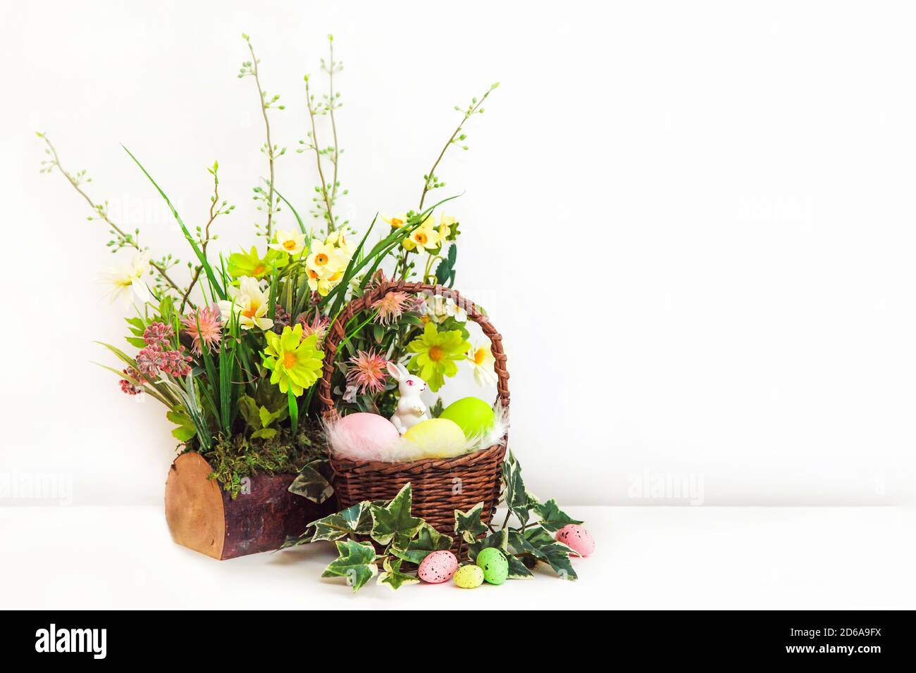 Buona Pasqua. Congratulazioni pasqua sfondo con copia spazio. Uova di Pasqua colorate e fiori con un piccolo coniglietto bianco in cestino. Stump con fiori. Foto Stock