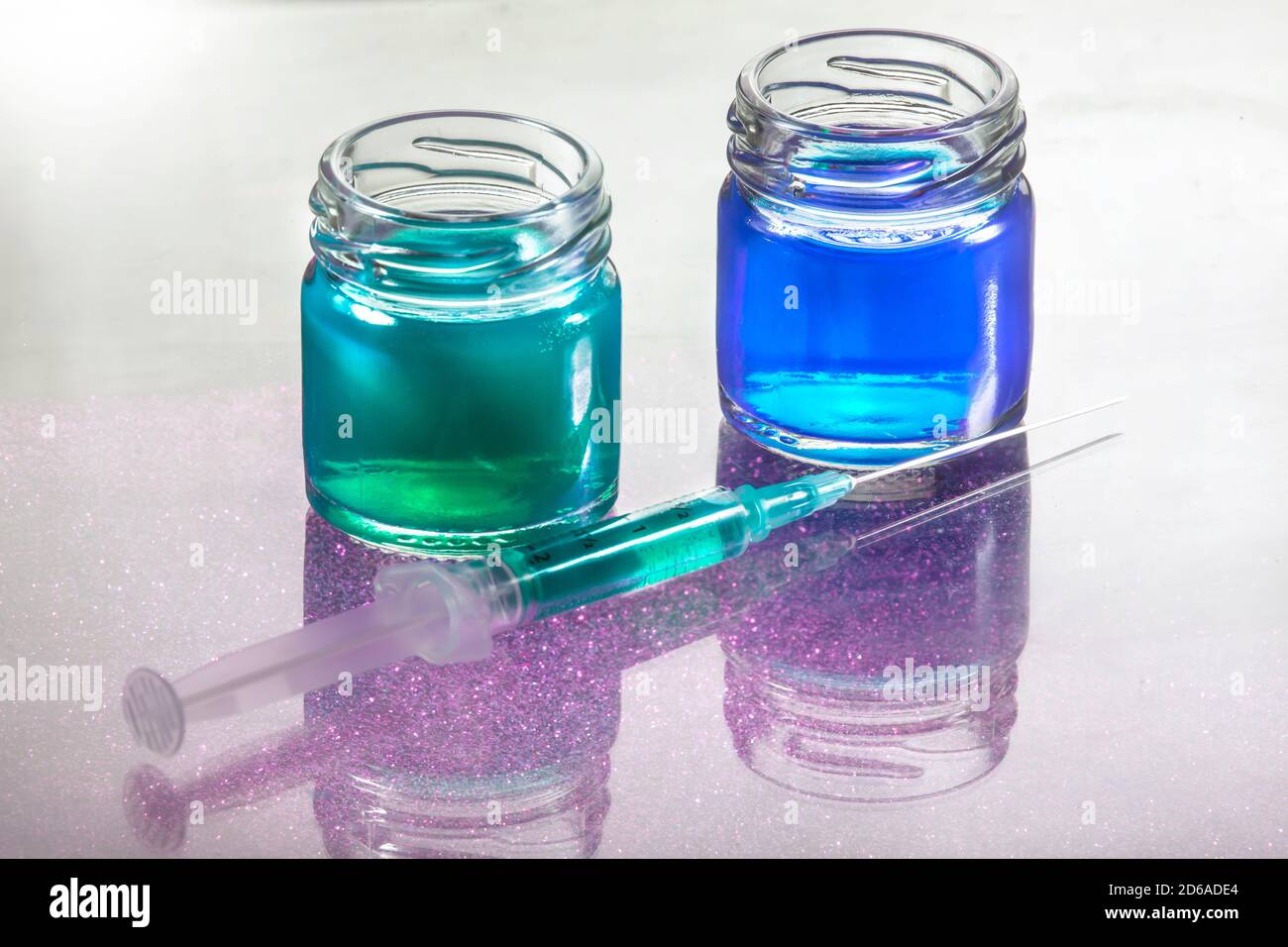 Primo piano Foto di contenitori in vetro liquido blu e verde con Siringa davanti a loro con ombra di grano viola Foto Stock