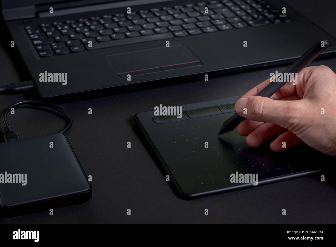 Disegnare a mano su un tablet con una penna con un computer portatile e. un disco rigido su sfondo nero Foto Stock