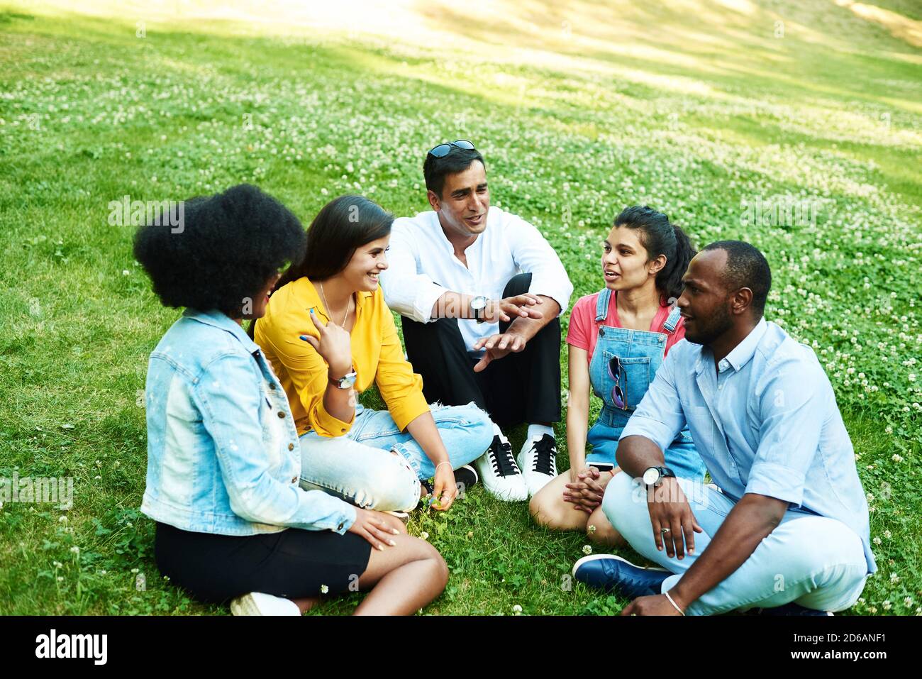 Afghani, neri, messicani e indiani che chiacchierano mentre si siede nel parco sull'erba. Il concetto di comunicazione di diverse nazionalità. Foto Stock