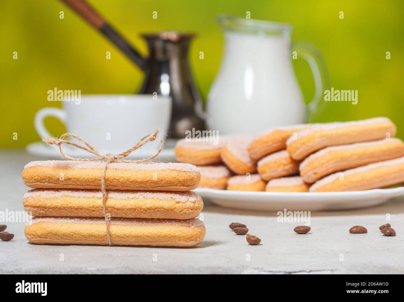Biscotti savoiardi italiani o biscotti ladybugs su un piatto e legati con una corda, una tazza bianca di caffè e una brocca di latte sullo sfondo. Selectiv Foto Stock