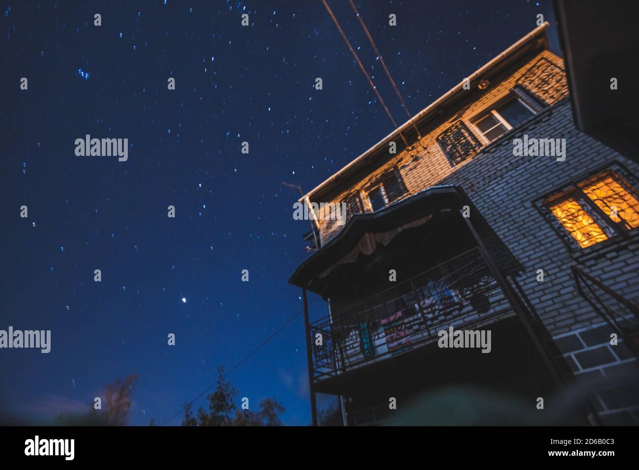 Foto notturna di una casa di campagna in mattoni con finestra illuminata solitaria con un cielo stellato su uno sfondo. Concetto di pace, magia, idilliaco, casa, sogni Foto Stock