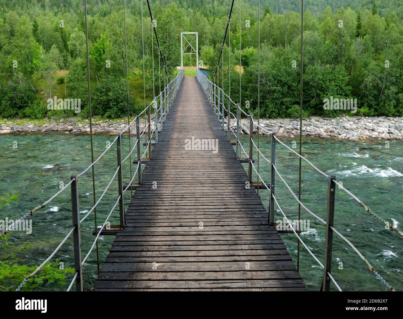 Attraversando UN ponte sospeso pedonale di legno sul fiume Ranaelva vicino MO i Rana Norvegia in un giorno estivo nuvoloso Foto Stock