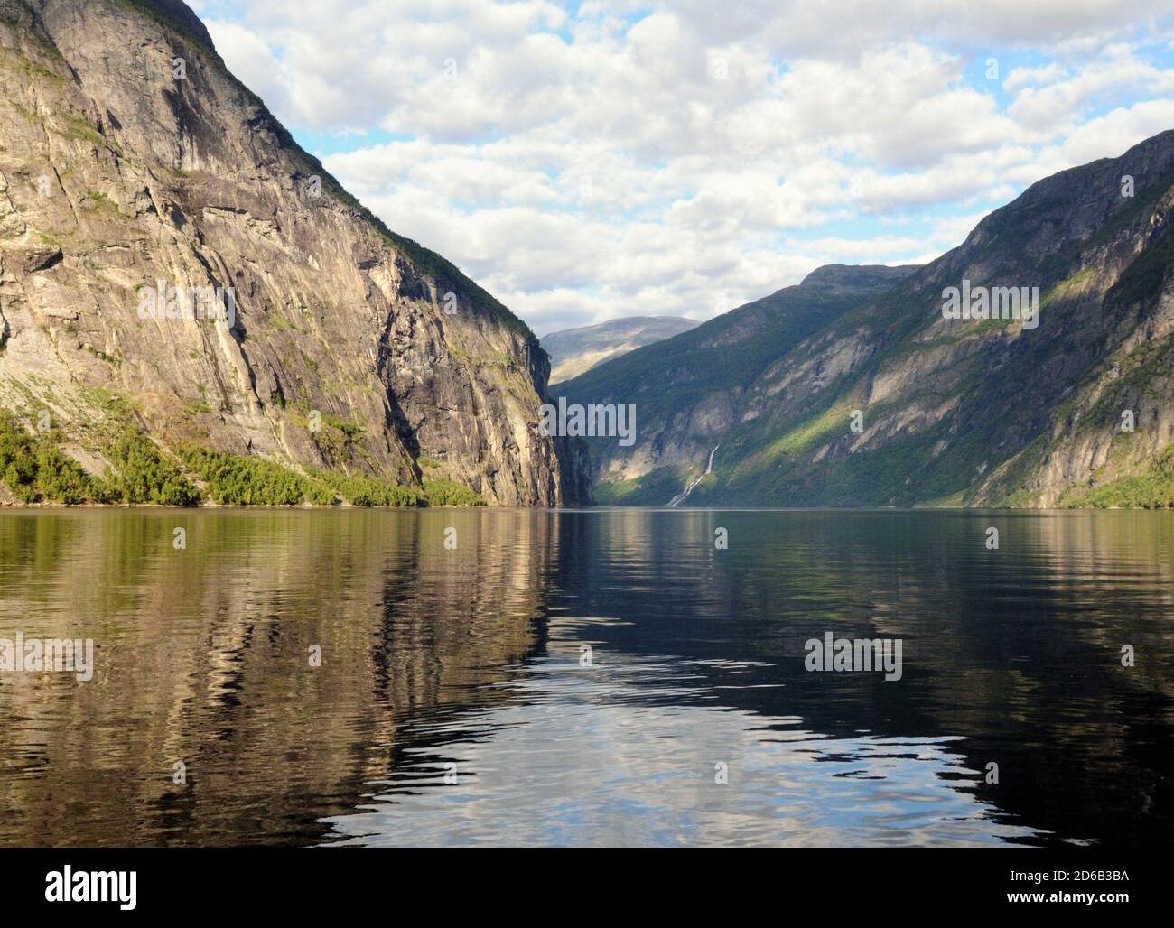 Montagne che si riflettono nelle acque calme del Geirangerfjord su UN Giorno estivo soleggiato con un cielo blu chiaro e UN Poche nuvole Foto Stock