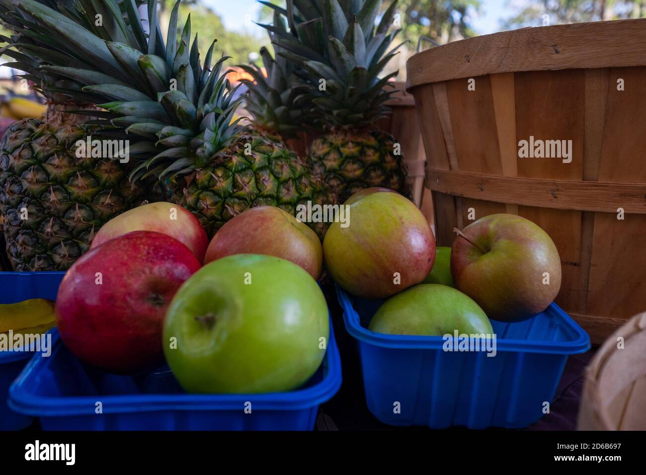 Due cestelli di plastica blu riempiti di mele fresche rosse e verdi. Ci sono più ananas interi sullo sfondo. Foto Stock