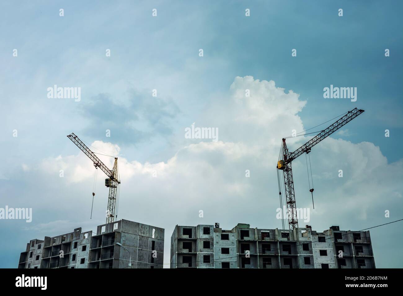 Gru sopra un edificio grigio a più piani incompiuto sullo sfondo di cielo blu nuvoloso con spazio per la copia. Processo di costruzione di condominio Foto Stock