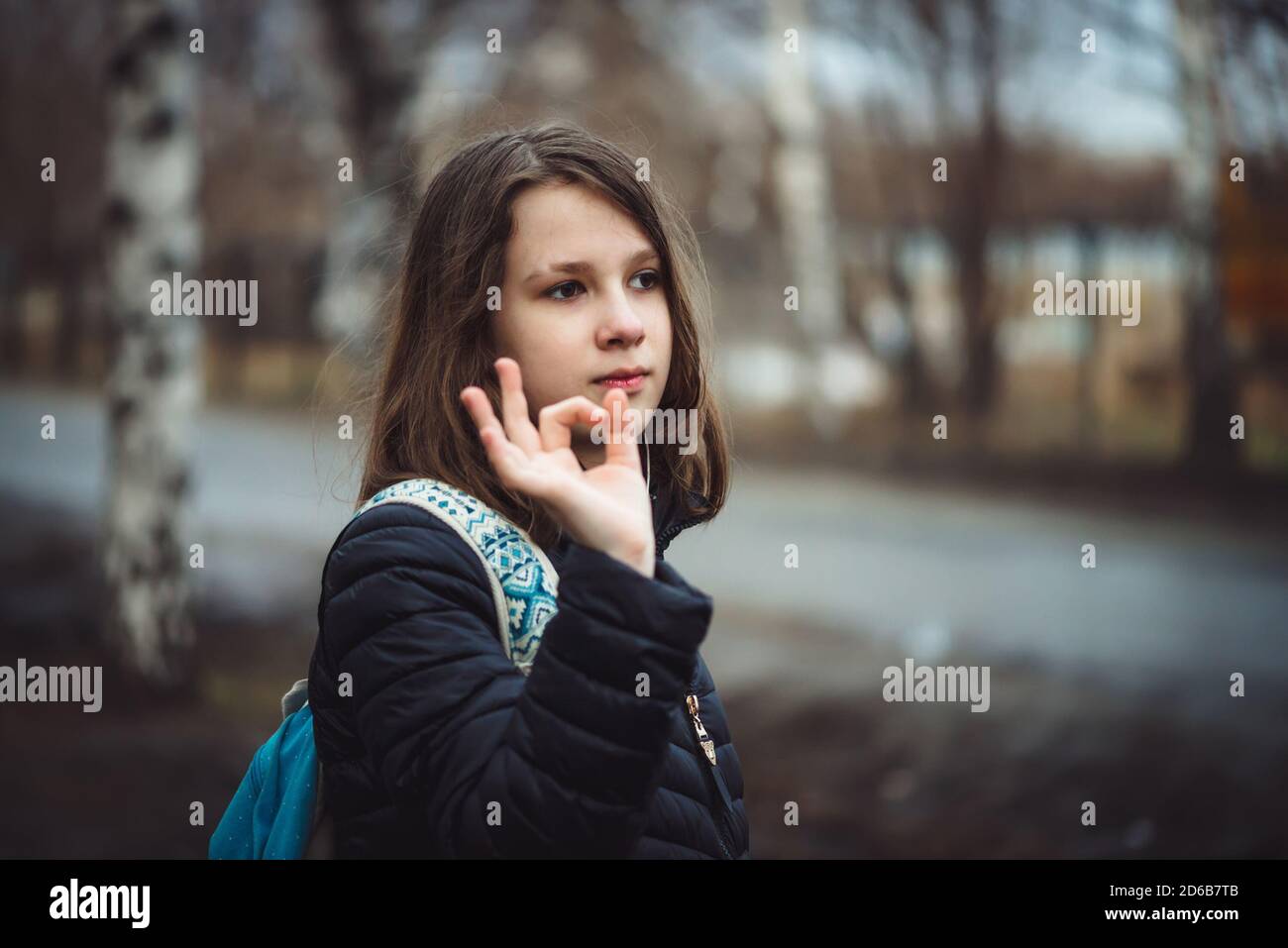Studentessa con zaino cammina in stato depresso lungo la strada della città in tempo nuvoloso in pioggia. Giovane ragazza con capelli bagnati in tonalità sbiadite è all'aperto con Foto Stock