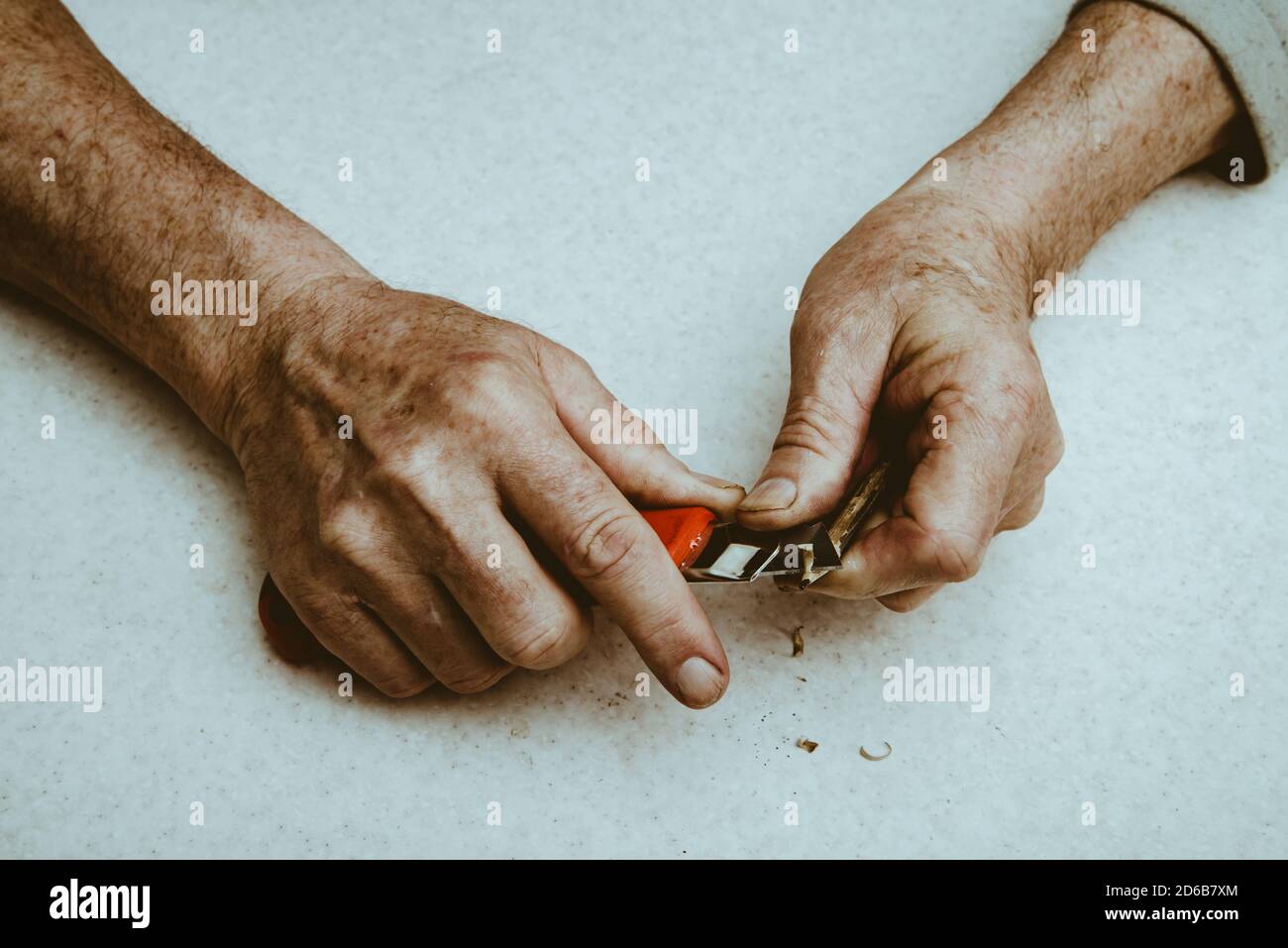 L'uomo anziano affila la matita con il coltello chierico. Le mani del vecchio uomo da vicino. Foto Stock