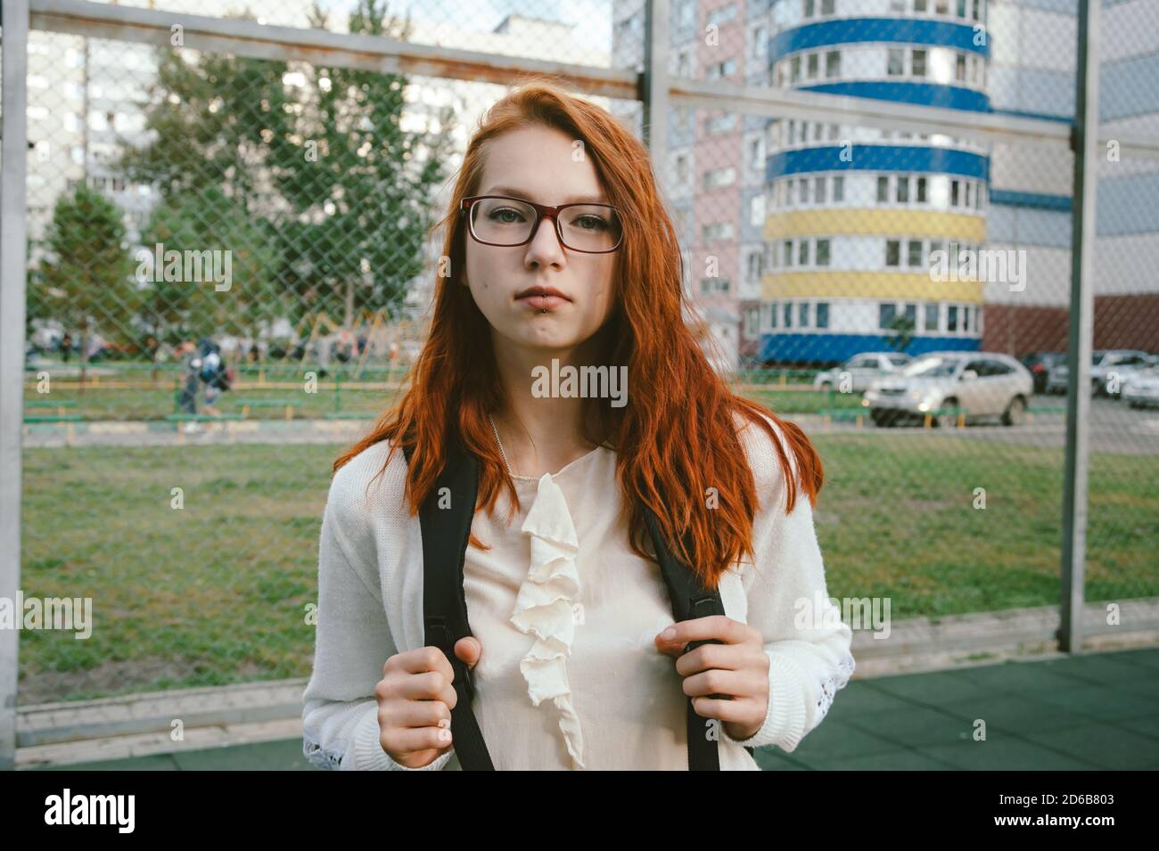 Ritratto di una ragazza sorridente dai capelli rossi con occhiali rossi sullo sfondo di edifici alti. Foto Stock