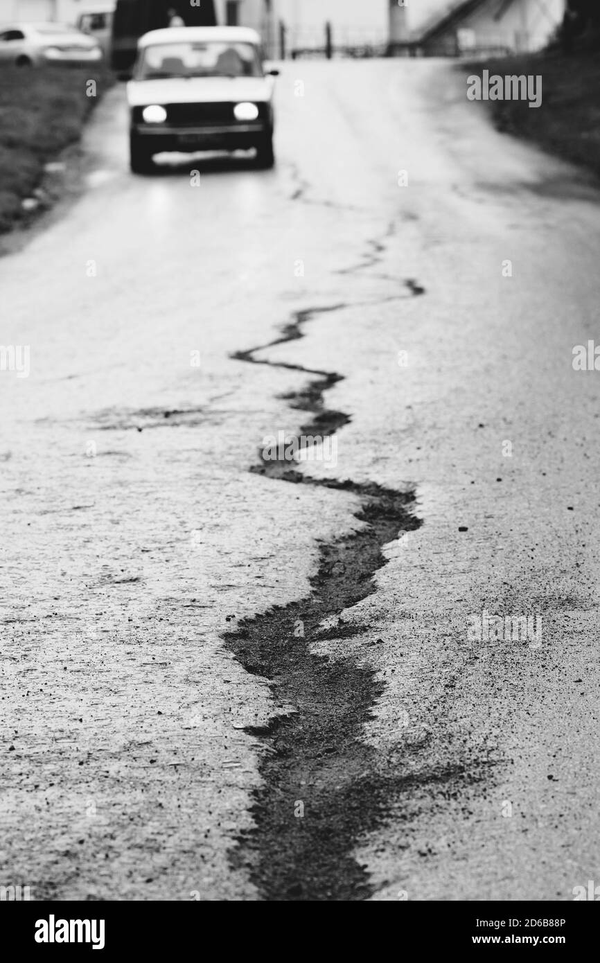 Un'incrinatura sull'asfalto e un'auto che viaggia davanti. Fotografia in bianco e nero. Concettuale. Foto Stock