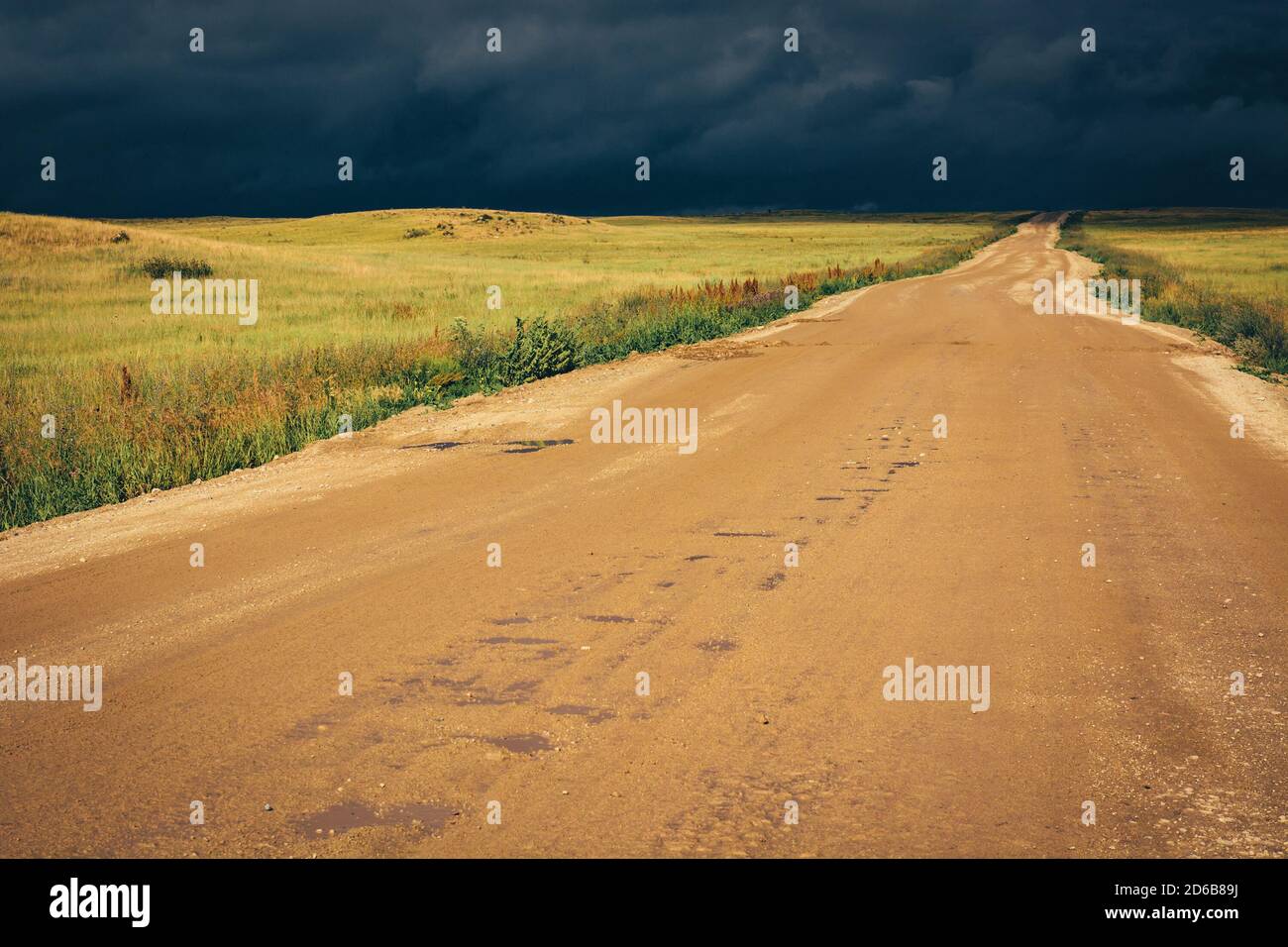 Strada sterrata fino alla linea dell'orizzonte sotto le drammatiche nuvole buie della tempesta. Foto Stock
