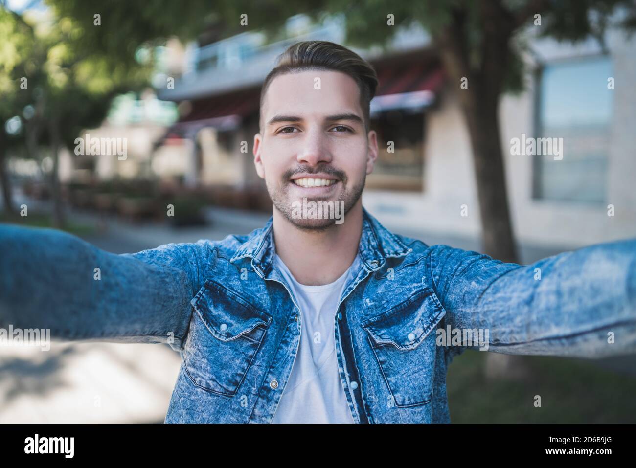 Ritratto di giovane bell'uomo che indossa abiti casual e prendendo un selfie all'aperto in strada. Foto Stock