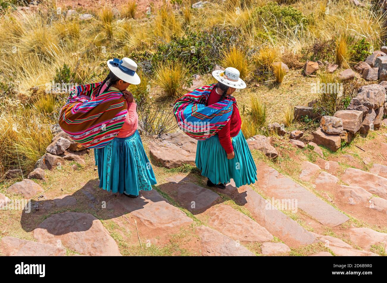 Due donne indigene di Quechua in abbigliamento tradizionale e tessuto camminando giù i gradini, l'isola di Taquile, il lago Titicaca, Puno, Perù. Foto Stock
