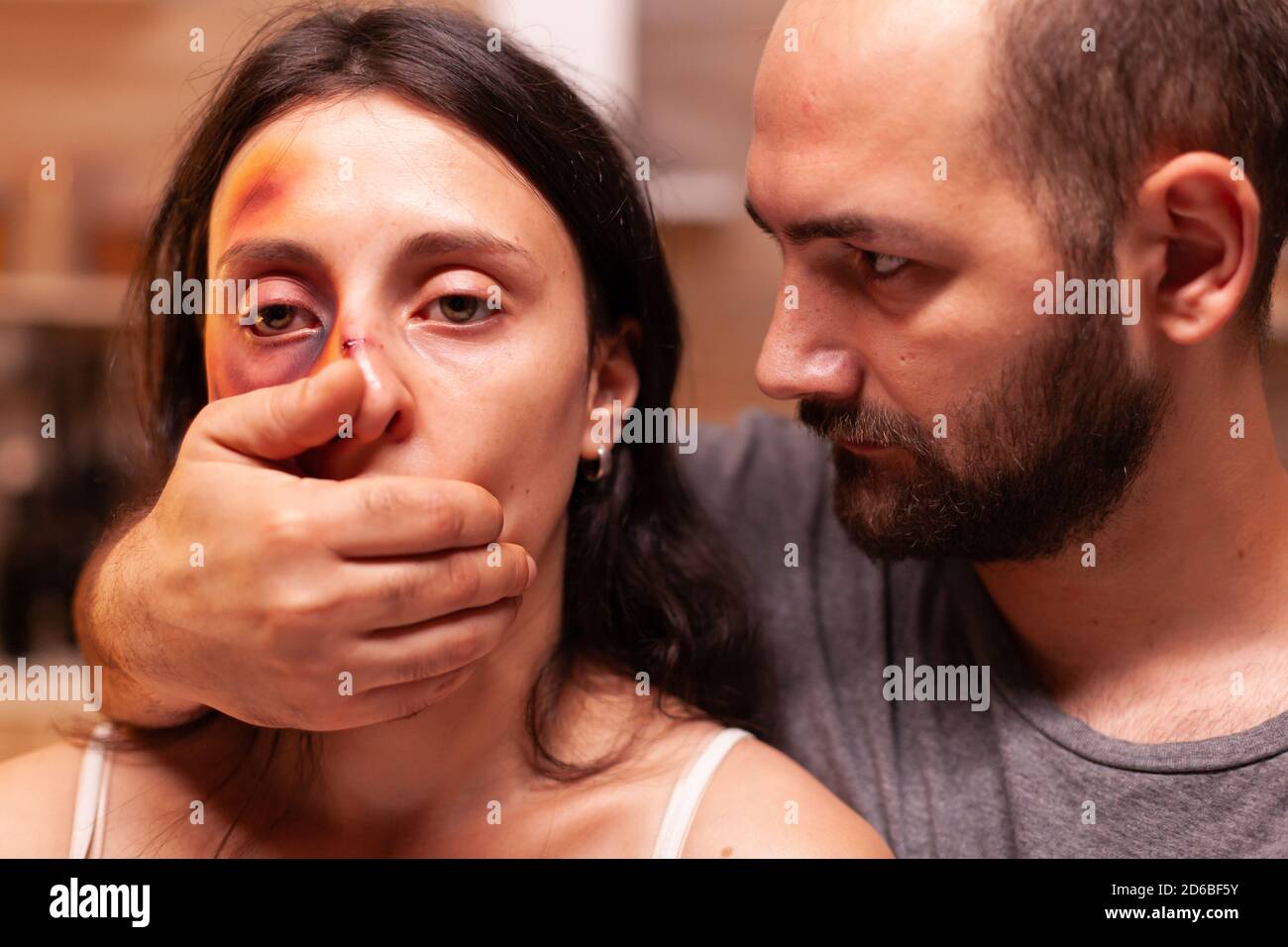 Violento marito che ricopre la bocca della moglie dopo aver battuto e livido il viso. Marito aggressivo che abusa ferendo terrorizzata donna impotente, vulnerabile, impaurita, picchiata e in preda al panico. Foto Stock