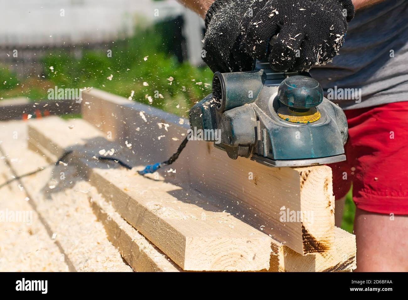 carpentiere mani in guanti piano elettrico piallare legname, trucioli volanti, segatura Foto Stock