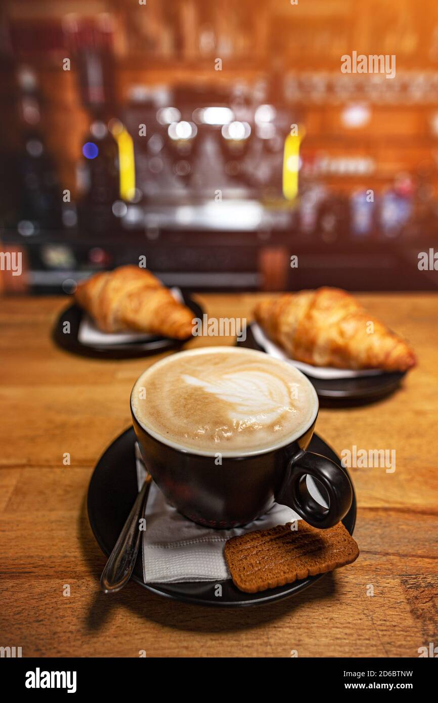 Tazza di caffè e croissant su tavolo di legno con sfocatura caffetteria come sfondo Foto Stock