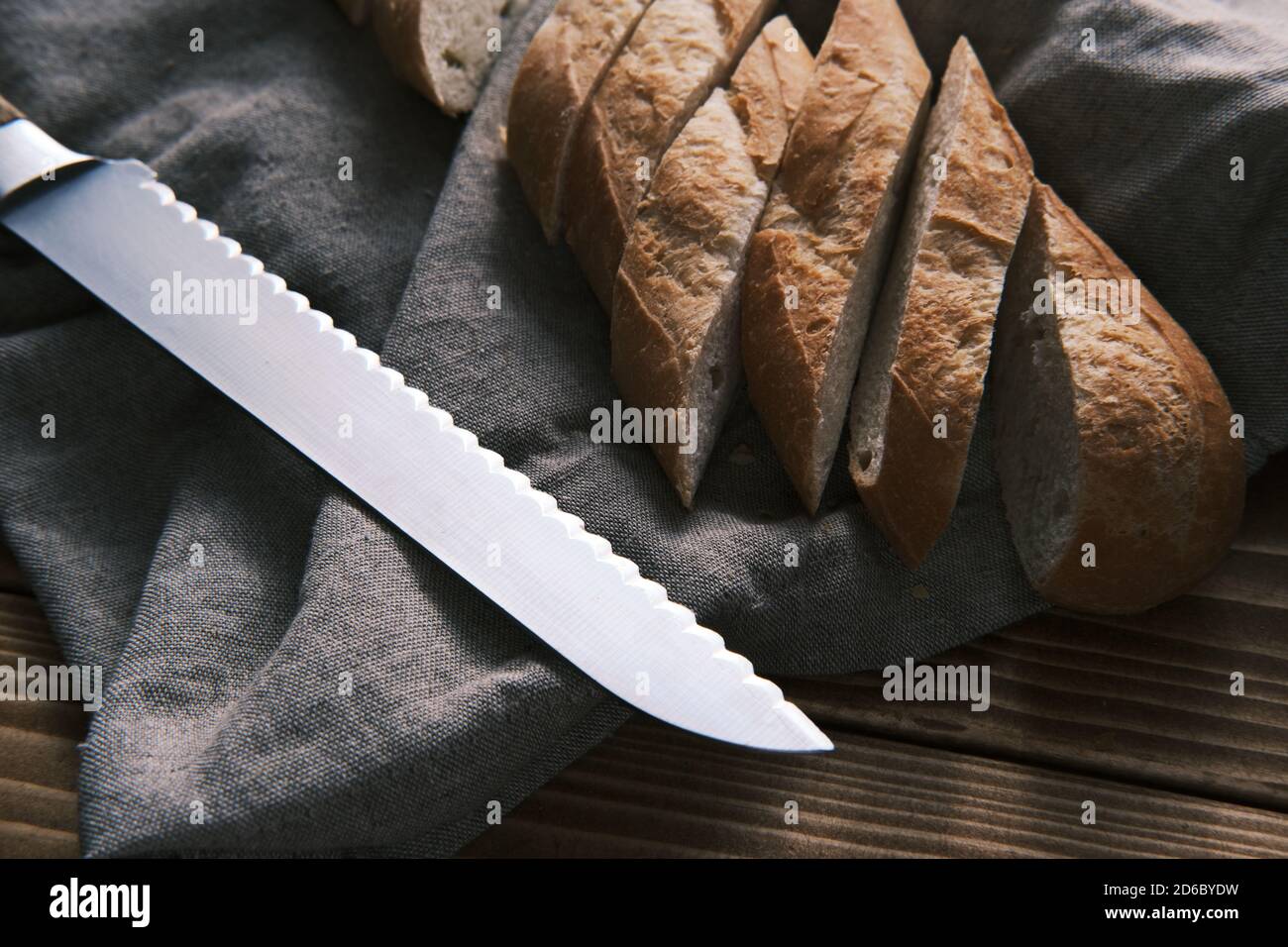 Primo piano baguette francese a fette fresche su un panno di lino con coltello su un tavolo di legno Foto Stock