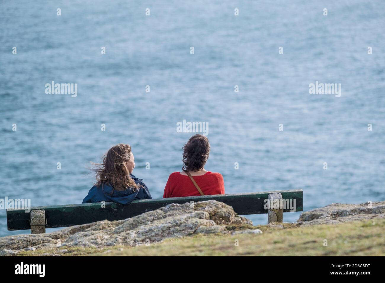 Due amici femminili seduti su una panchina che si affaccia sul mare sulla costa di Newquay in Cornovaglia. Foto Stock