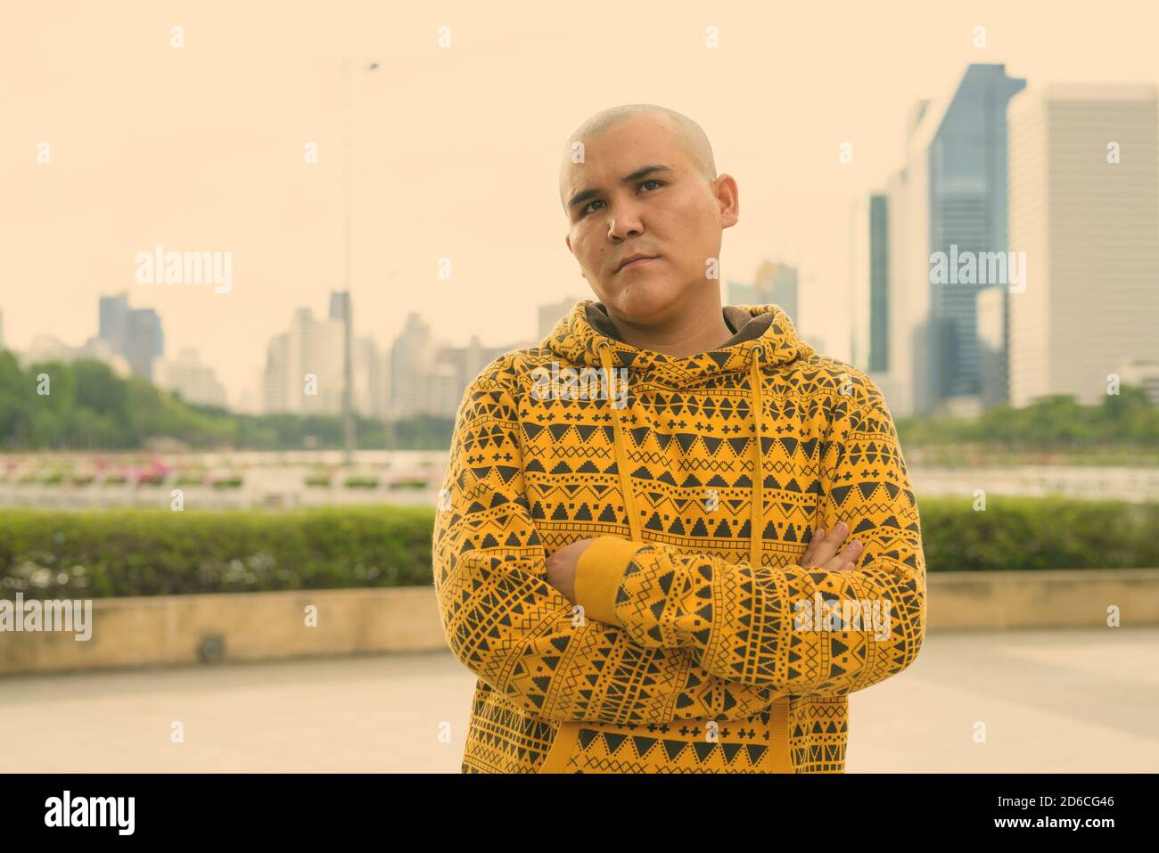 Giovani asiatici calvo uomo contro la vista della città al parco Foto Stock