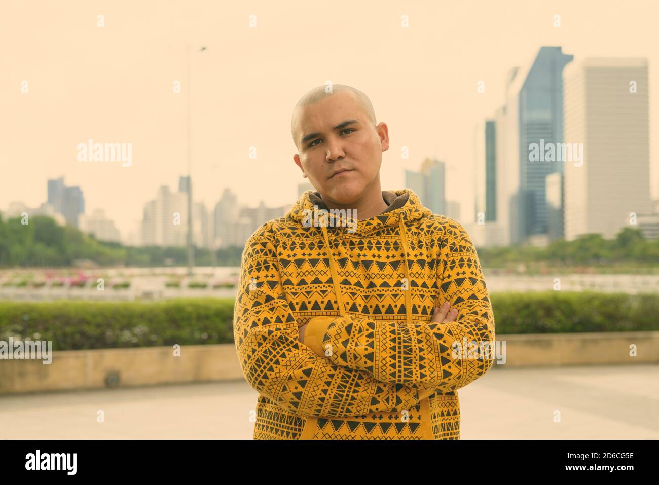 Giovani asiatici calvo uomo contro la vista della città al parco Foto Stock