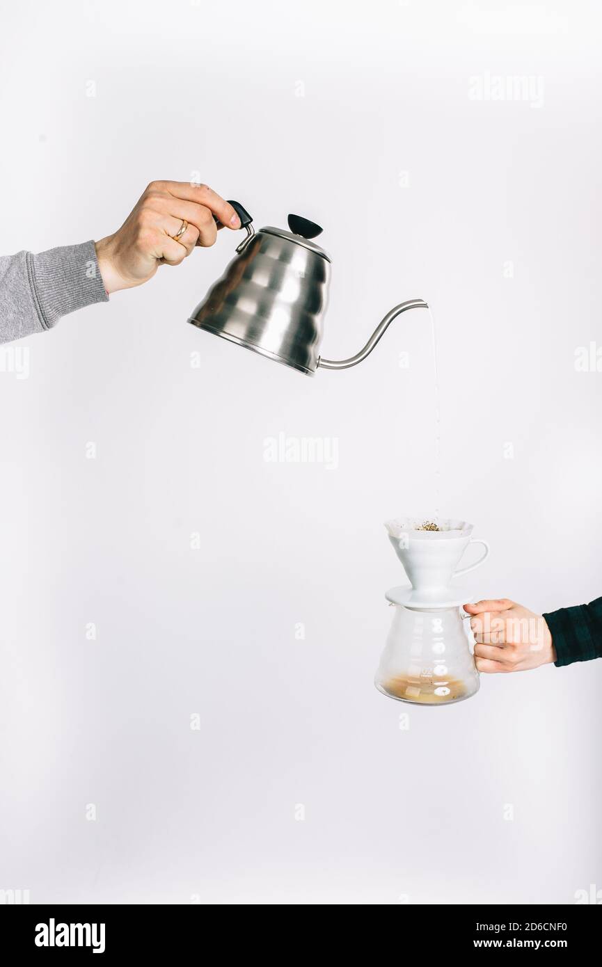 Le mani umane su uno sfondo bianco versano il caffè attraverso un filtro speciale. Foto Stock
