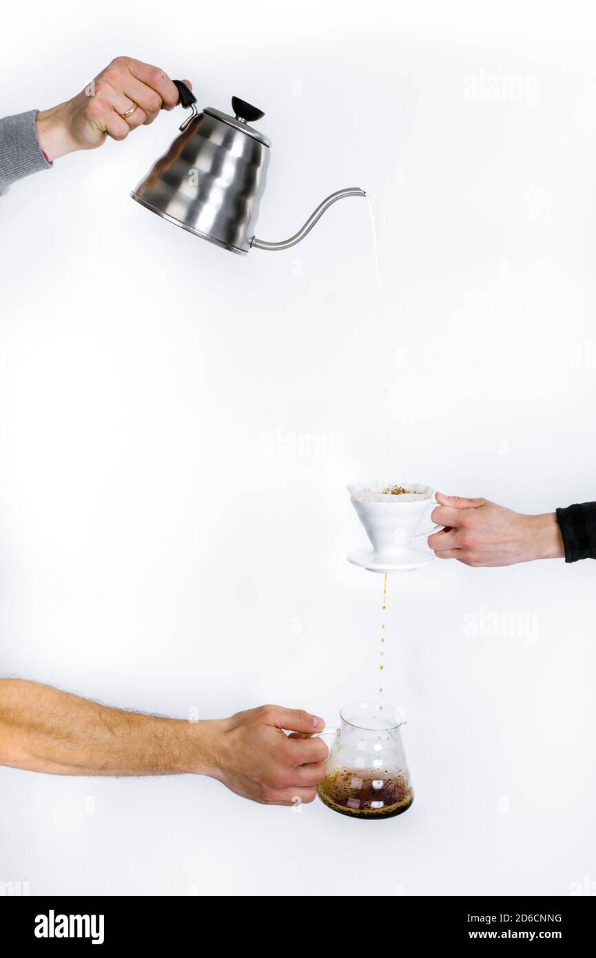 Le mani umane su uno sfondo bianco versano il caffè attraverso un filtro speciale. Foto Stock