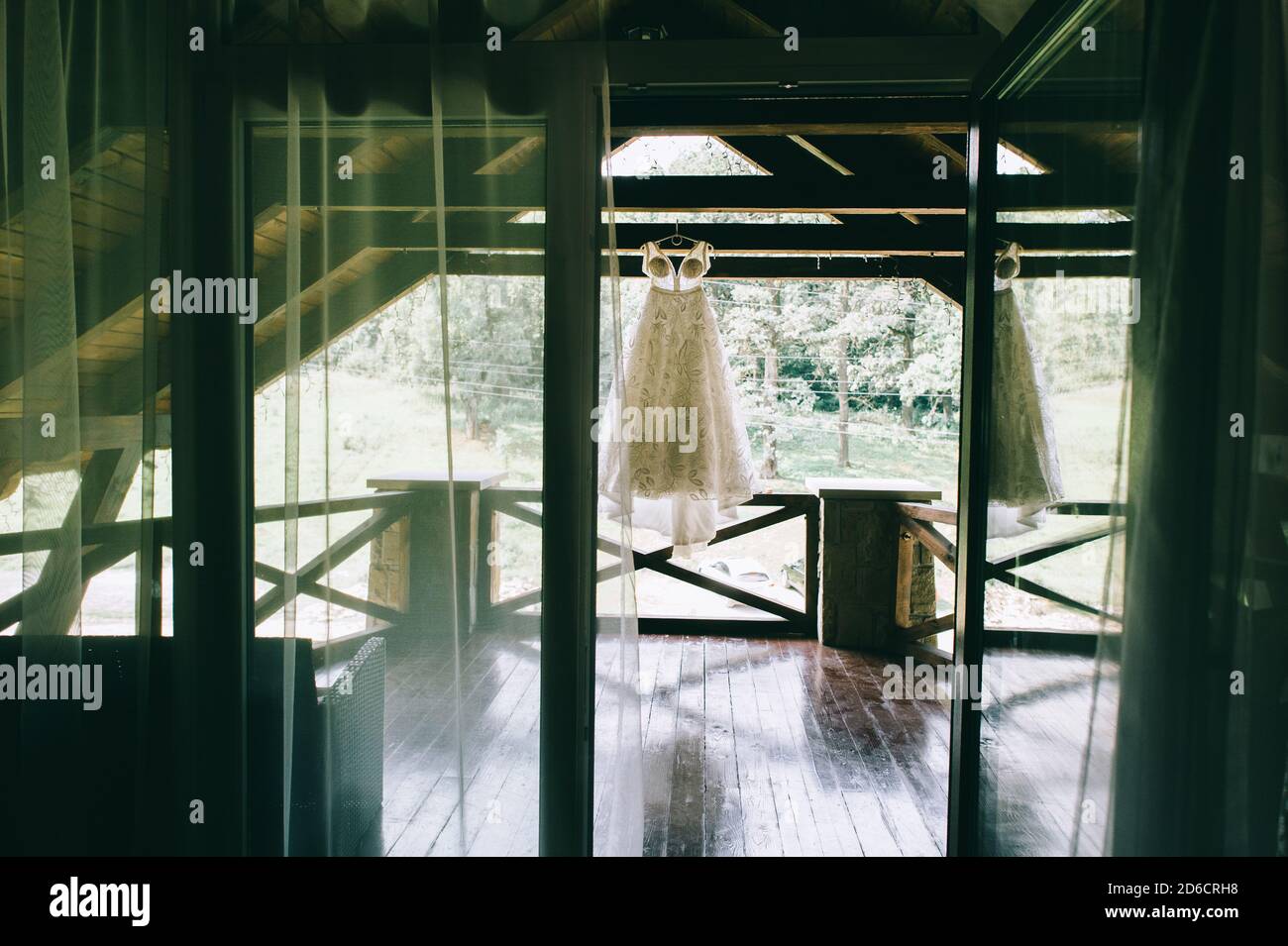 Vista attraverso la finestra aperta su un elegante abito da sposa originale appeso su un appendiabiti sulla terrazza. Foto Stock