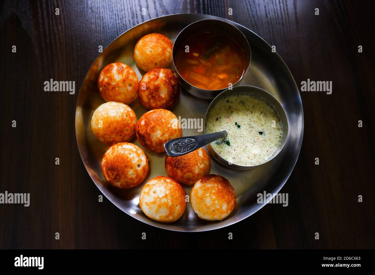 Una vista dall'alto del tradizionale paddu dell'India del sud (appe di riso) con sambar, chutney isolato in piastra su tavolo di legno Foto Stock