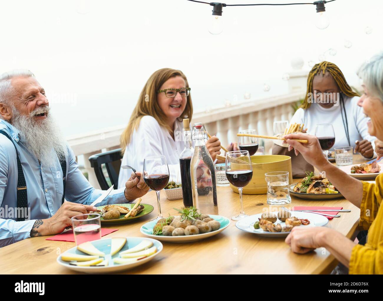 Anziani multirazziali che cenano insieme sulla terrazza della casa - anziani Divertirsi a cena sul patio della casa - cibo e. concetto di bevanda Foto Stock