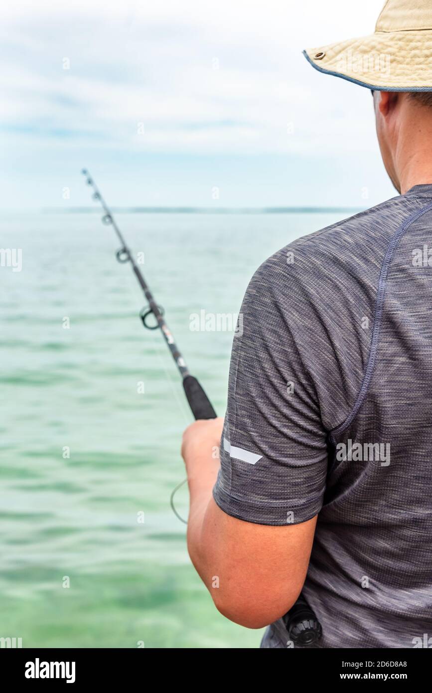 Uomo asiatico in un cappello solare che tiene una canna da pesca, la pesca nel mare turchese con terra e l'orizzonte in lontananza. Florida Keys, Stati Uniti. Foto Stock