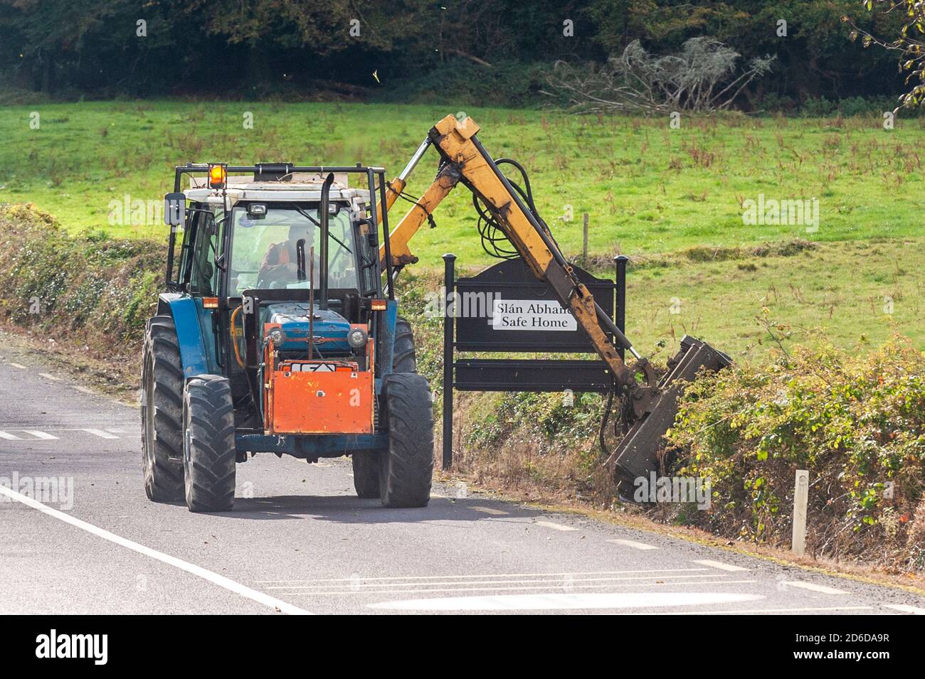 Agricoltore che taglia una siepe con un trattore e una taglierina a West Cork, Irlanda. Foto Stock