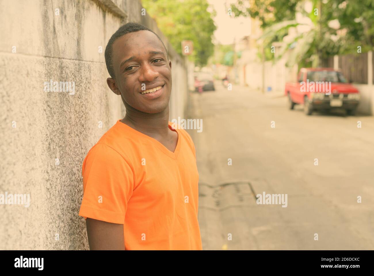 Giovani felici Africano nero uomo sorridente mentre il pensiero e appoggiata contro il vecchio muro di cemento nelle strade all'aperto Foto Stock