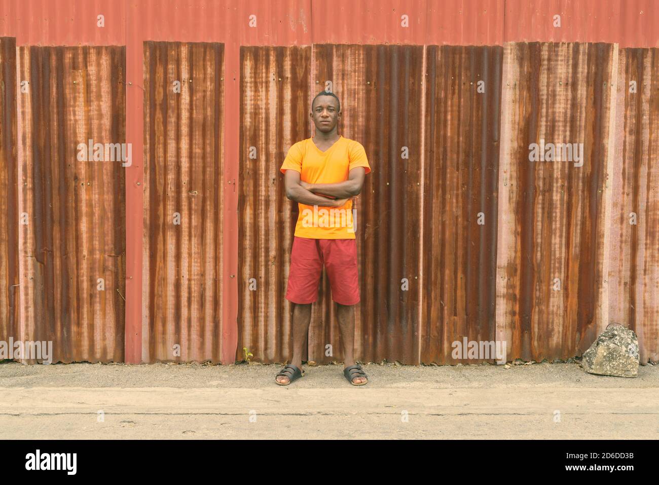 Giovane Africano nero uomo in piedi con le braccia incrociate contro il vecchio arrugginito parete del foglio Foto Stock