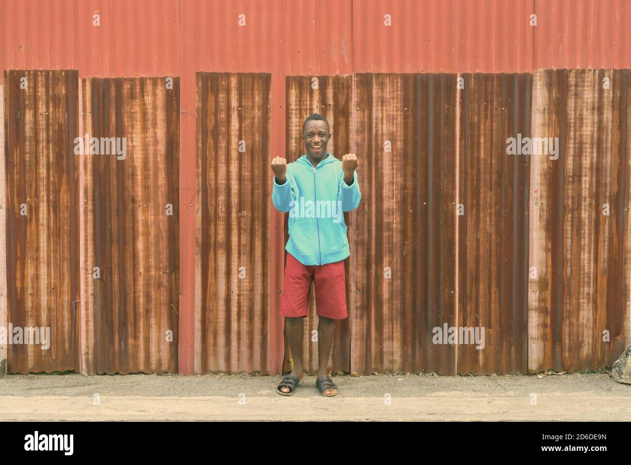Giovani felici Africano nero uomo sorridente mentre lo sguardo eccitato mentre in piedi contro il vecchio arrugginito parete del foglio Foto Stock
