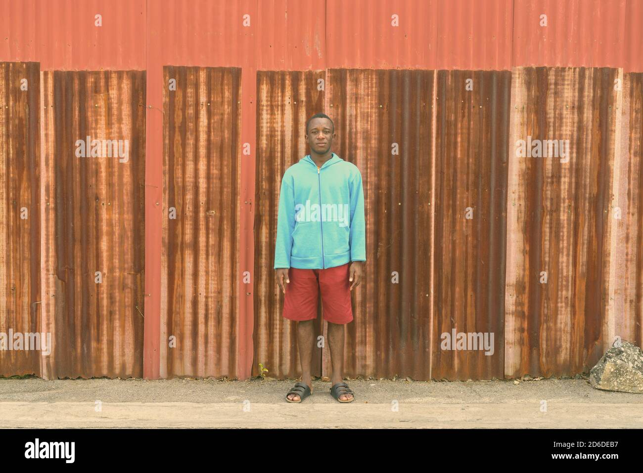 Giovane Africano nero uomo in piedi contro il vecchio arrugginito parete del foglio Foto Stock