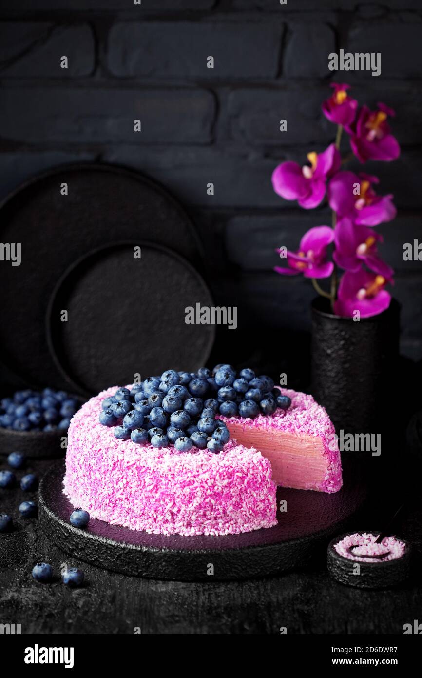 Torta crepe fatta in casa con panna pitahaya rosa al cocco e mirtilli freschi su sfondo nero, fuoco selettivo Foto Stock