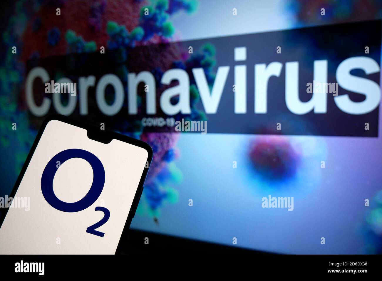 Il logo O2 visualizzato su un telefono cellulare con un modello illustrativo del Coronavirus visualizzato su un monitor sullo sfondo. Foto Stock