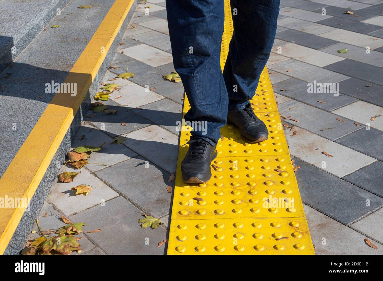 Uomo che cammina su blocchi gialli di pavimentazione tattile per ciechi handicap.blocchi di Braille, piastrelle tattili per ipovedenti, Tenji Blocks.Textured Foto Stock