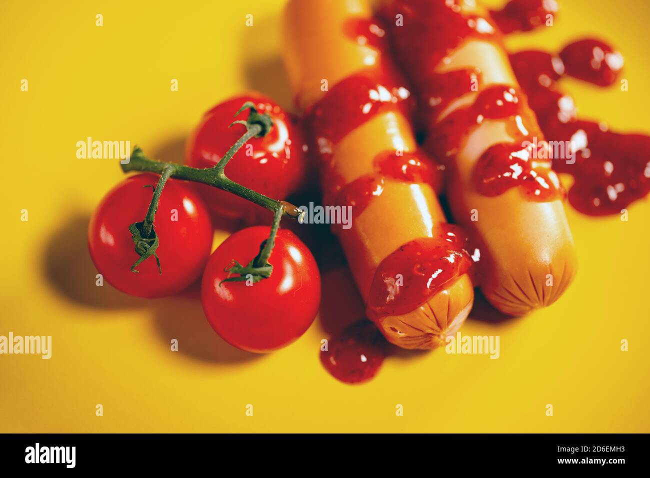 Primo piano di salsicce in salsa con pomodori ciliegini. Appetitosi frankfurters con piccoli pomodori rossi e ketchup su sfondo giallo. Foto Stock