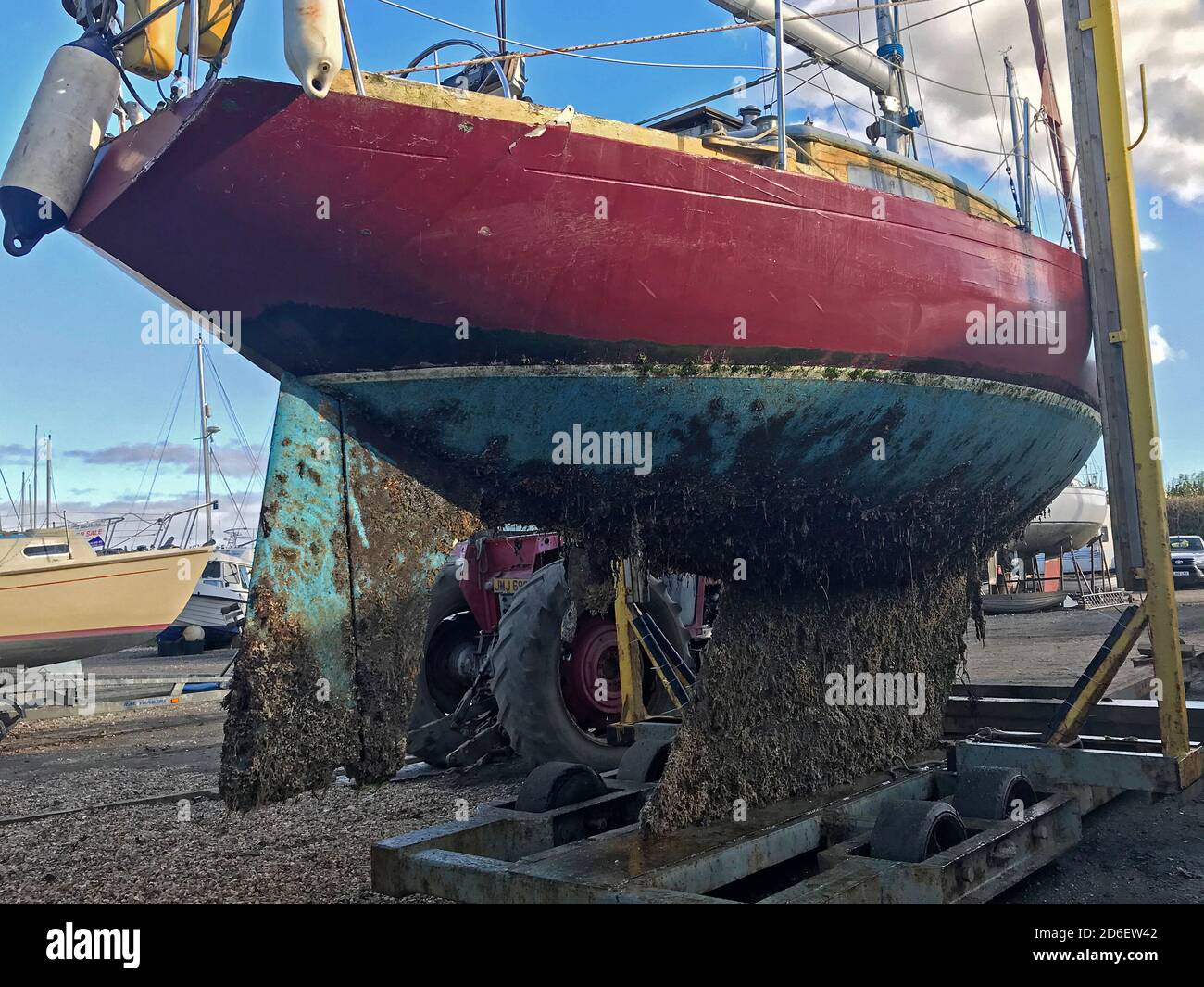 Yacht con eccessiva crescita marina sul suo scafo grp culla per scivoli da cantiere pronta per lavaggio e raschiatura a getto spento durante la manutenzione invernale Foto Stock