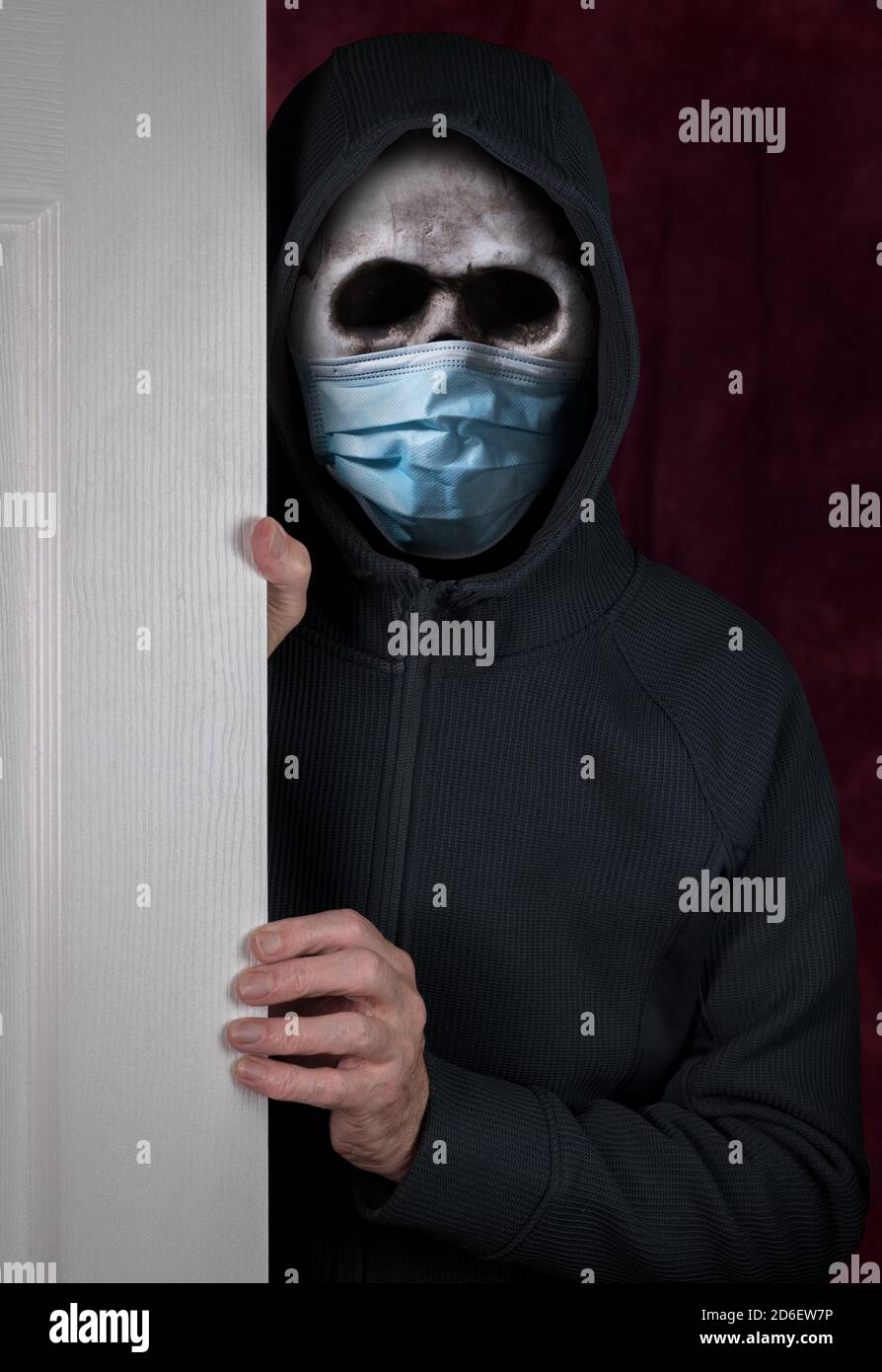Stalker o burglar entrare in una casa attraverso la porta con indossare un cranio umano dotato di maschera medica contro il coronavirus pandemia Foto Stock
