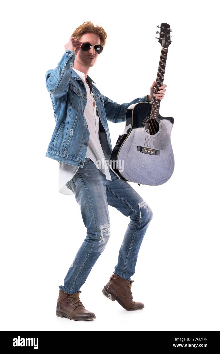 Giovane uomo rosso sicuro in jeans in posa con chitarra acustica che tiene occhiali da sole. Corpo intero isolato su sfondo bianco. Foto Stock